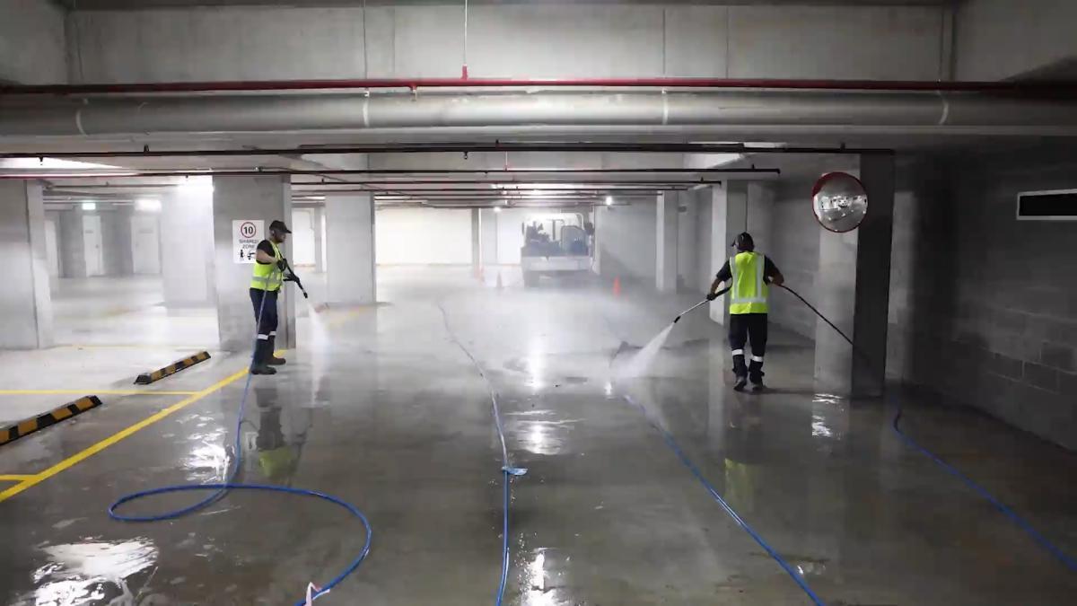 Two workers in high-visibility vests using high-pressure jetting equipment to clean an underground car park floor