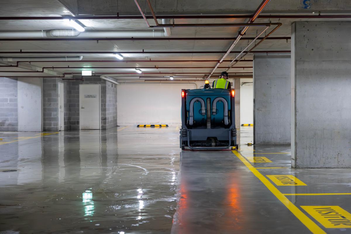 Industrial floor scrubber machine cleaning a multi-storey car park with wet concrete floor and yellow markings