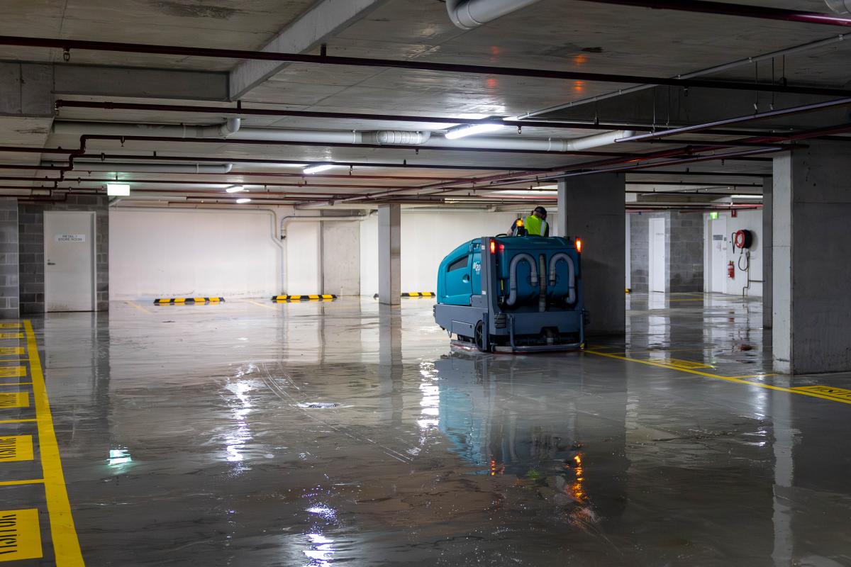 Industrial floor scrubbing machine cleaning wet concrete car park floor with operators in high-visibility clothing