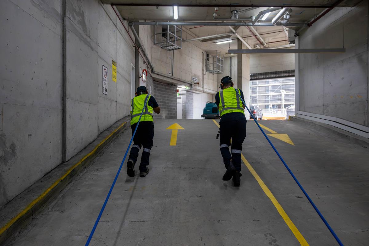 Two workers in high-visibility vests using pressure washing equipment to clean a car park surface
