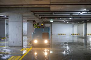 Industrial floor scrubber machine cleaning wet concrete surface in underground car park with operator in high-visibility clothing