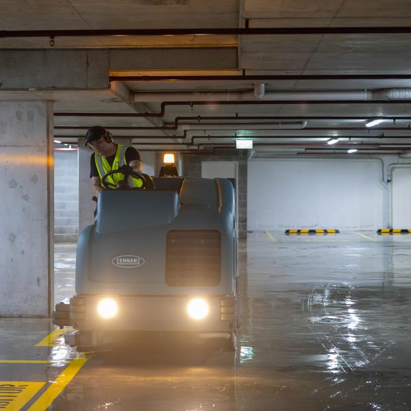 Worker operating industrial floor cleaning machine in underground car park with wet concrete floor