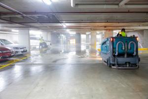 Industrial floor scrubber machine cleaning wet concrete in multi-level car park with parked vehicles