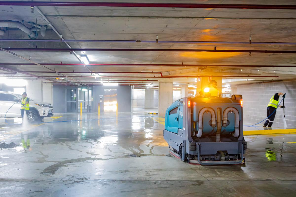 Professional car park cleaning service with high-pressure jetting equipment and workers in safety vests