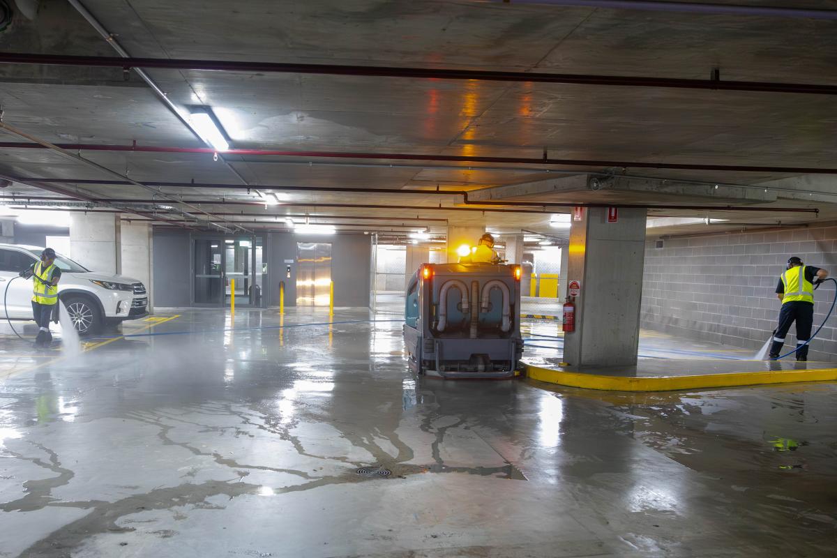 Professional car park cleaning team using high-pressure jetting equipment on wet concrete floor