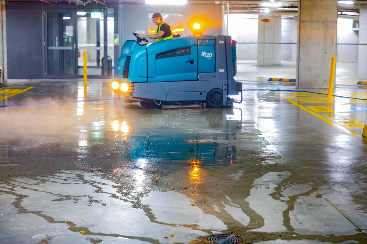 Industrial floor scrubber machine cleaning wet car park surface with operator in safety gear