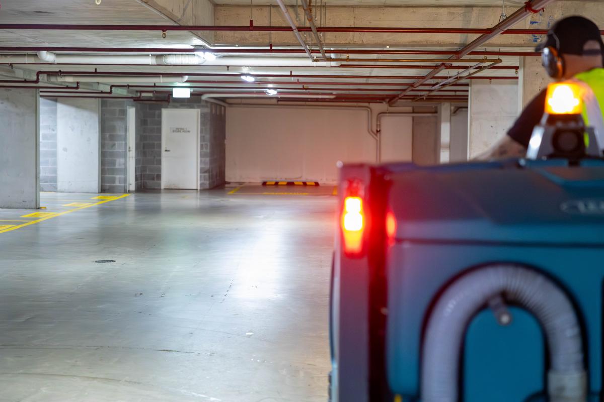 Industrial car park maintenance worker operating floor cleaning machine in underground parking facility