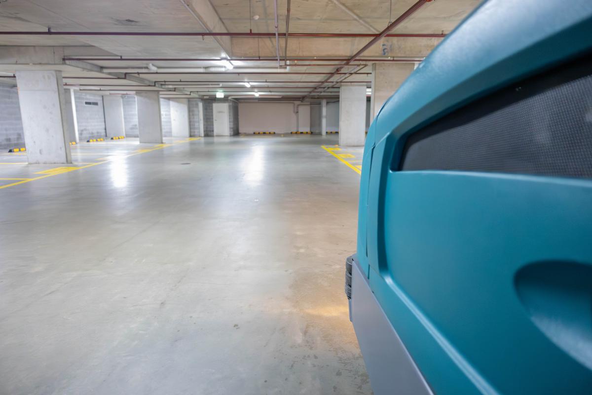 Underground car park with blue vehicle in foreground and clean concrete floor with yellow parking markings