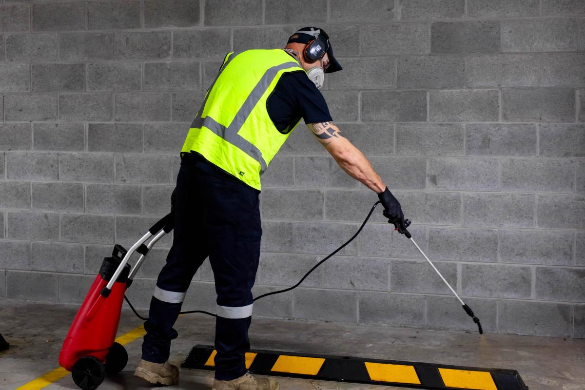 Industrial worker using high-pressure cleaning equipment on concrete floor with safety gear