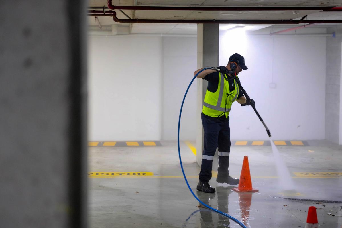 Worker in high-visibility gear using high-pressure jetting equipment to clean underground car park concrete floor