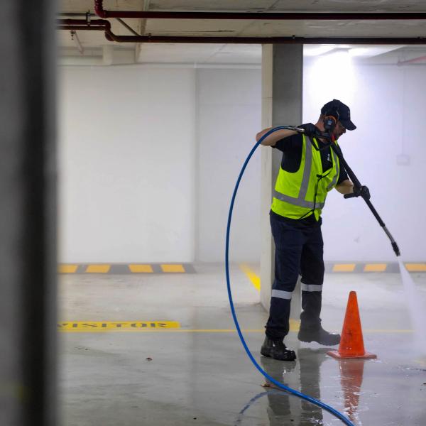 Worker in high-visibility gear using high-pressure jetting equipment to clean underground car park concrete floor