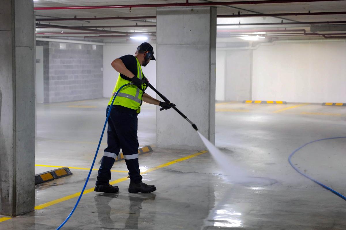 Professional worker using high-pressure jetting equipment to clean underground car park concrete floor