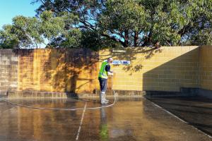 Worker in high-visibility clothing using high-pressure cleaning equipment on wet concrete surface