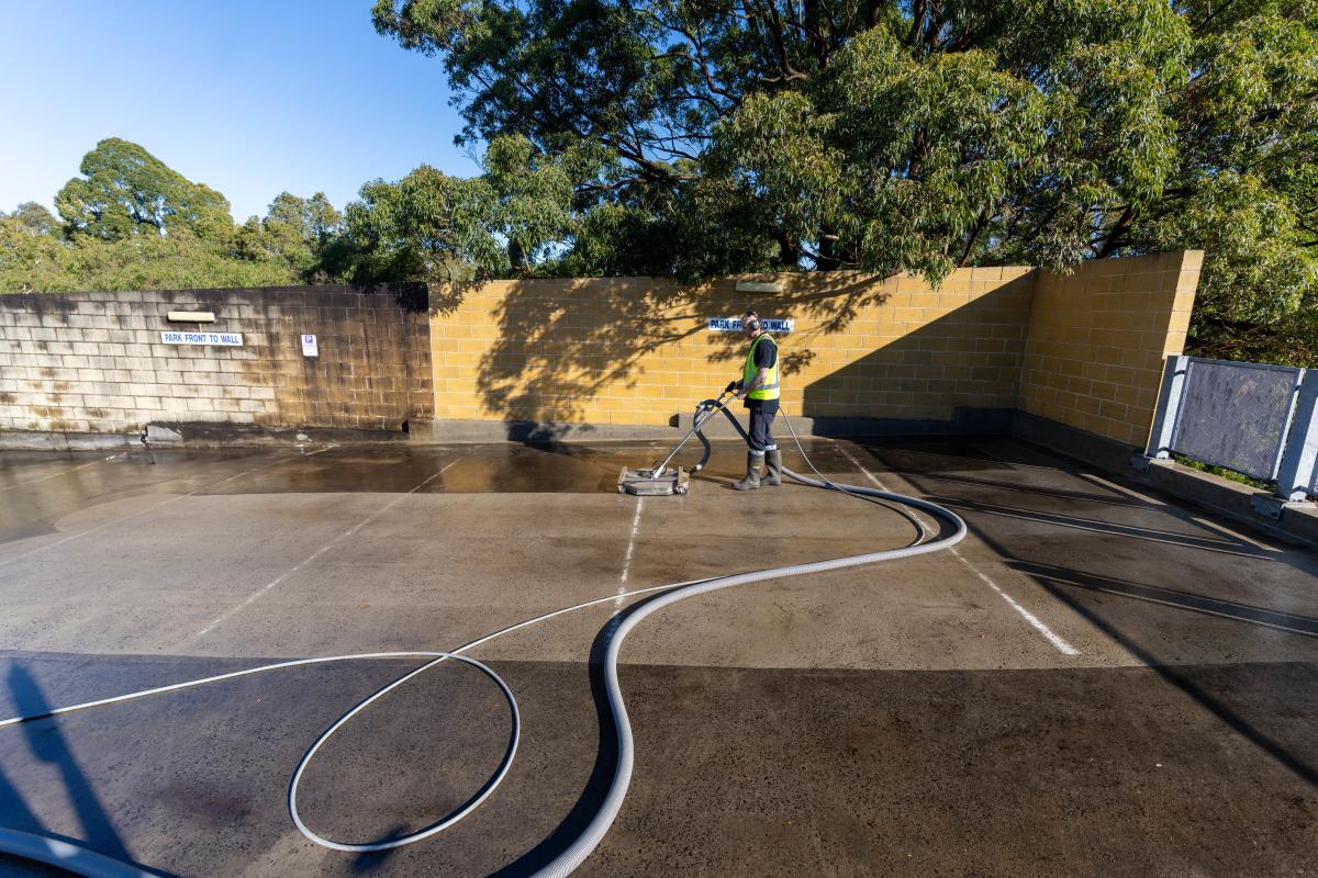 High-pressure cleaning equipment spraying water on large concrete surface near waterfront