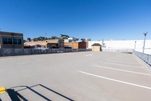 Empty car park with white line markings and commercial buildings in background under clear blue sky