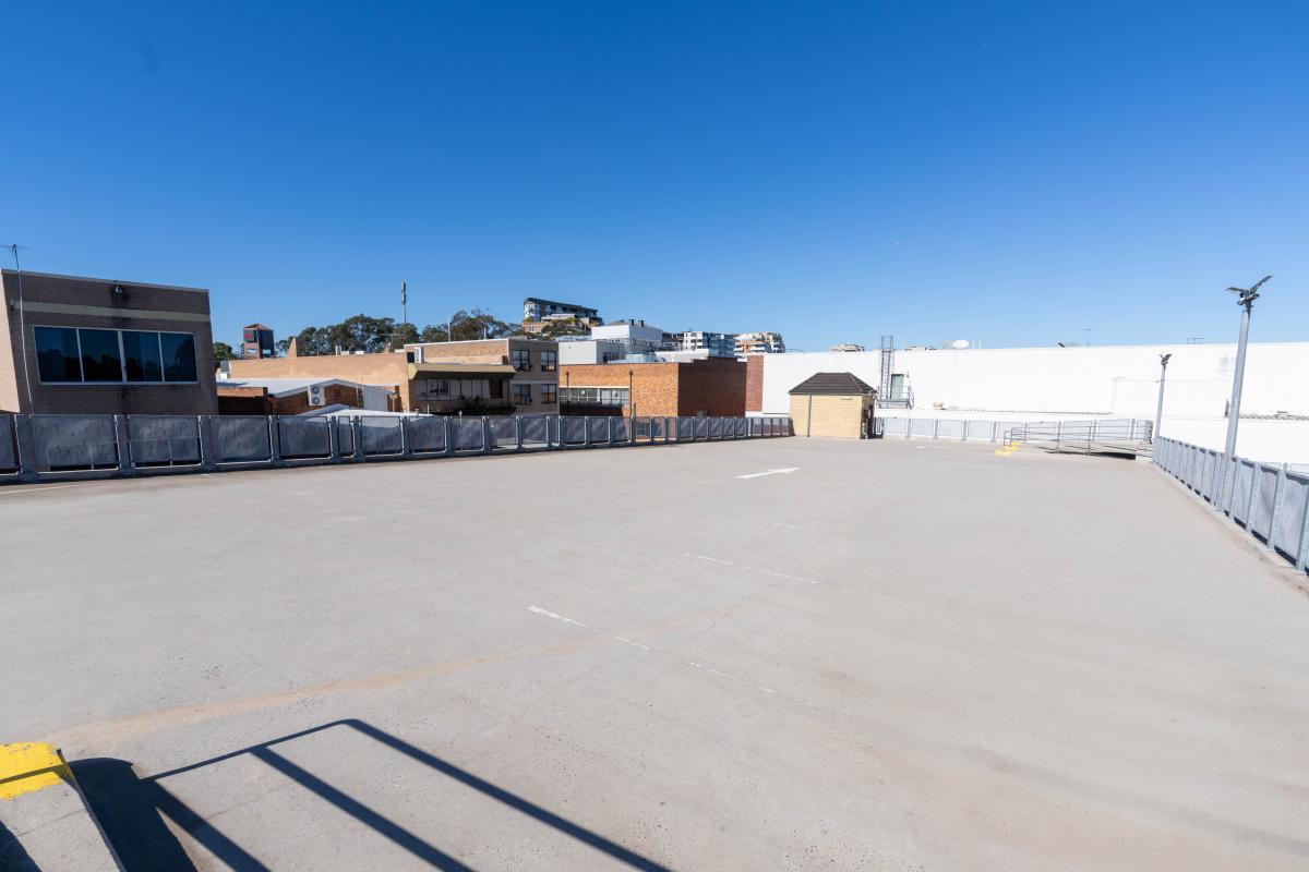 Empty concrete car park surface with industrial buildings and clear blue sky in background
