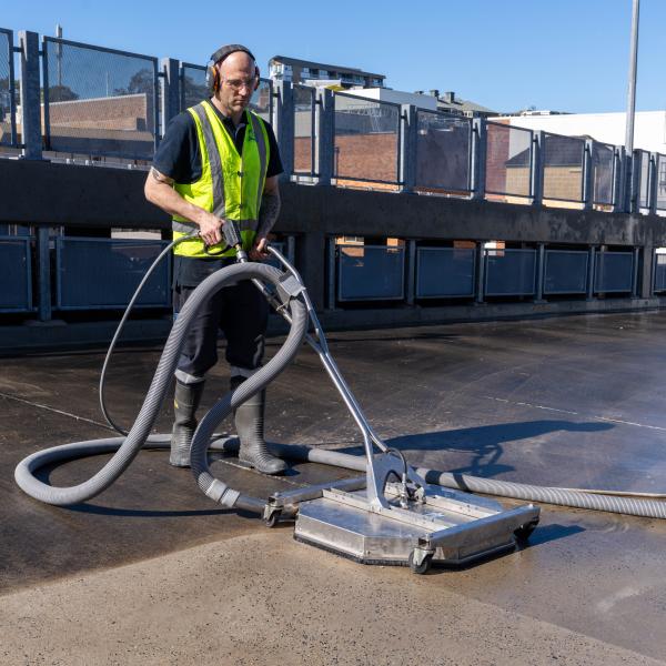 Worker in high-visibility clothing operating high-pressure cleaning equipment on warehouse concrete floor