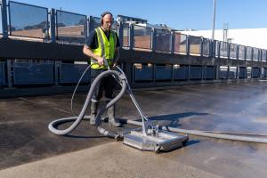 Worker in high-visibility clothing operating high-pressure cleaning equipment on warehouse concrete floor