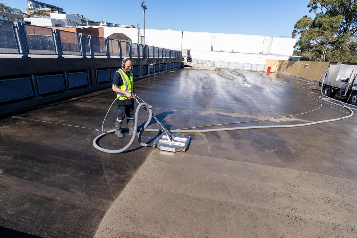 Worker operating high-pressure cleaning equipment on industrial warehouse concrete floor