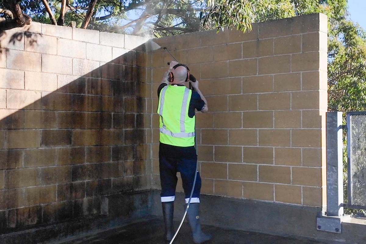 Worker in high-visibility vest using high-pressure jetting equipment to clean brick wall