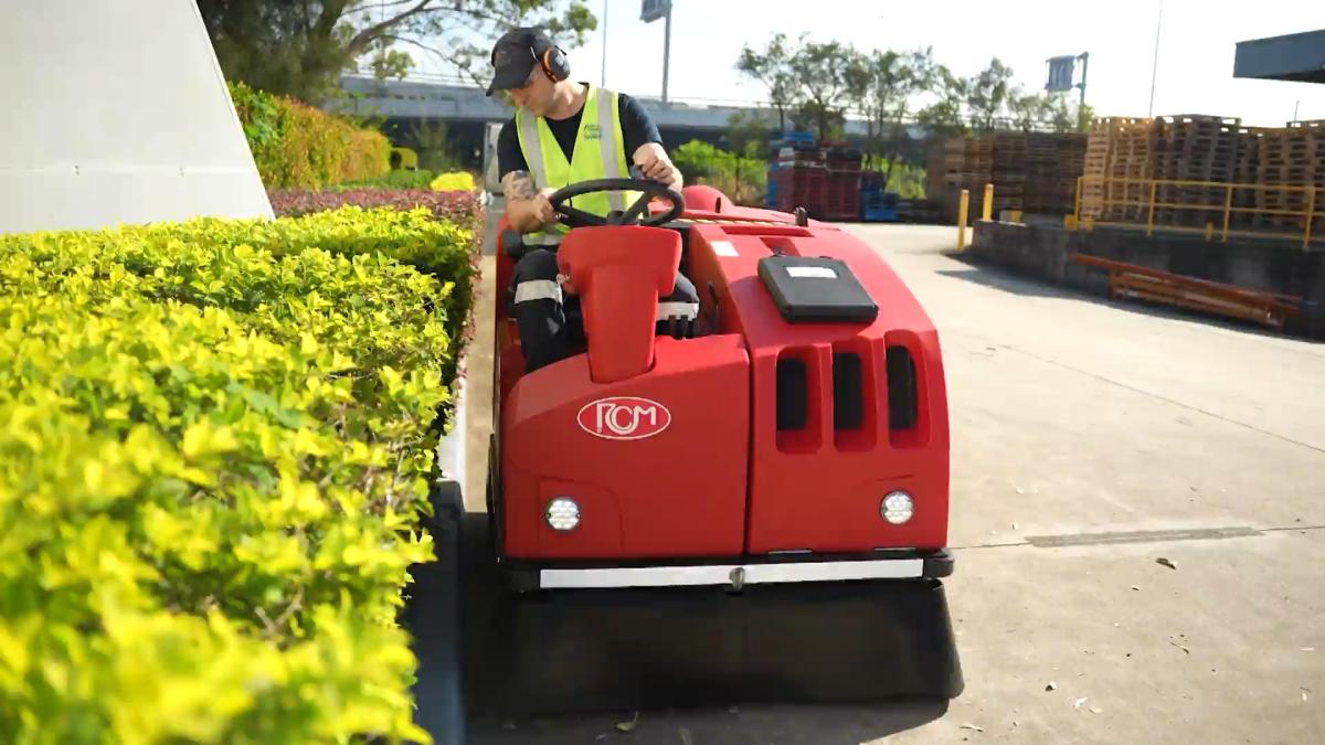 Professional operator using red floor cleaning machine in industrial facility car park