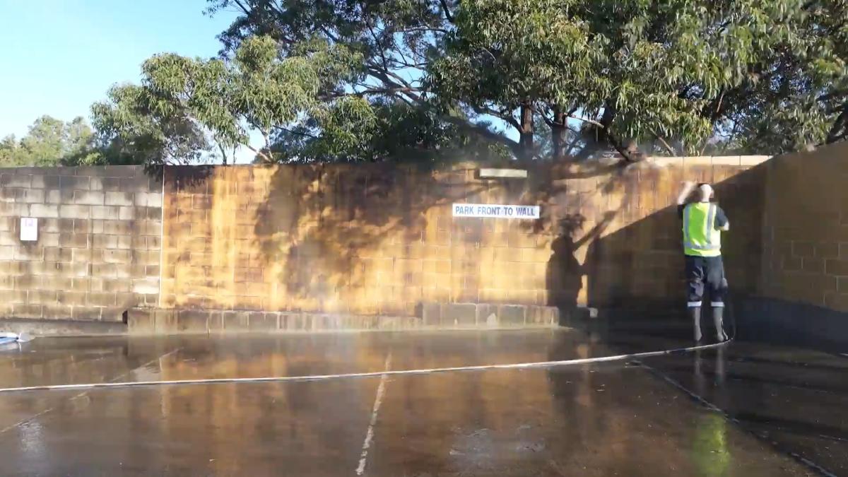 Professional high-pressure cleaning of brick wall in car park with worker in high-visibility vest
