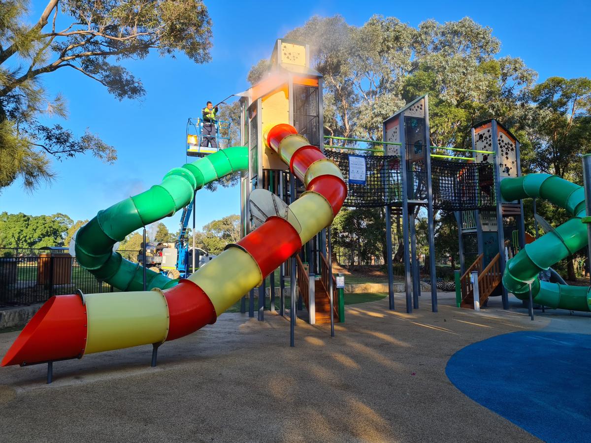 Colourful playground with multiple slides, climbing structures, and blue safety surface on sunny day