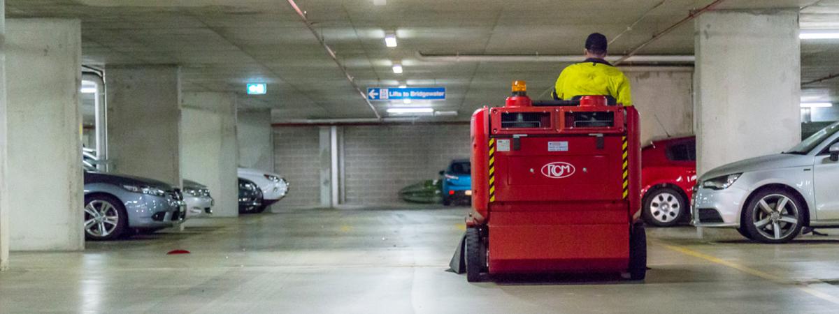 Underground car park cleaning with red industrial floor scrubber machine and operator in high-visibility clothing