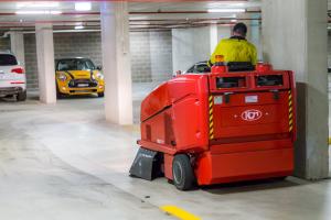 Professional floor scrubber machine cleaning underground car park with parked vehicles in background