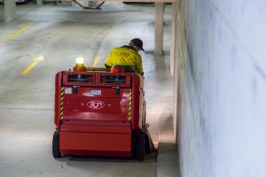 Worker operating red industrial floor scrubber machine in underground car park