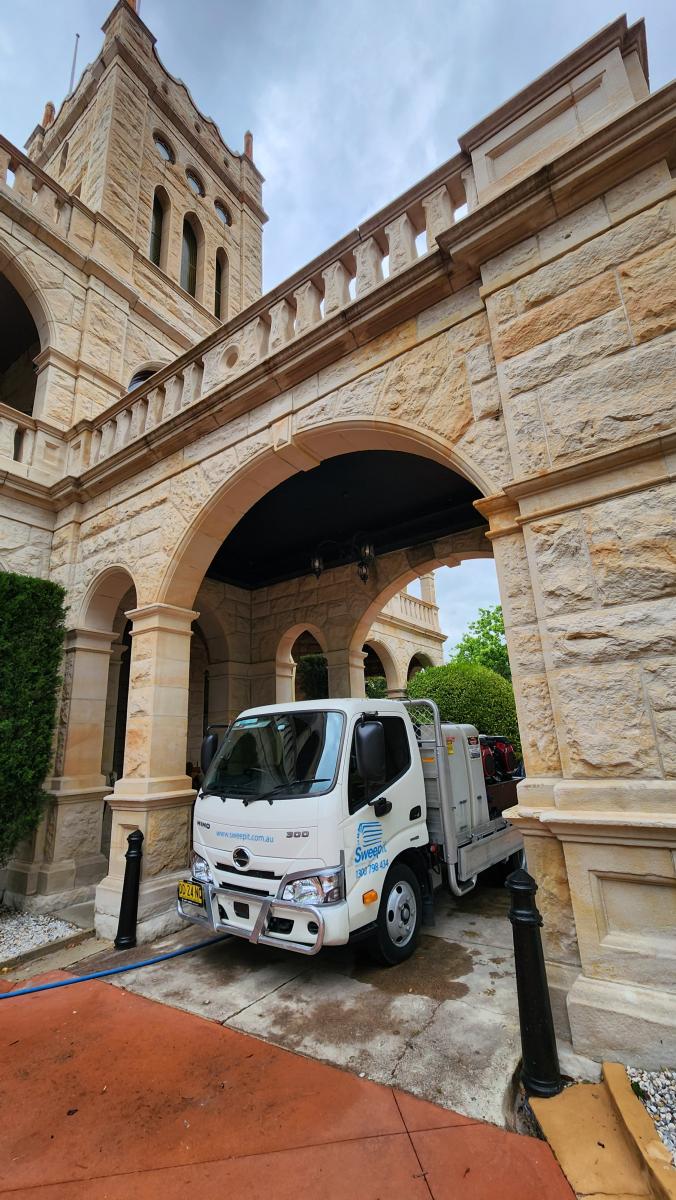 Professional cleaning vehicle parked beneath historic sandstone building archway