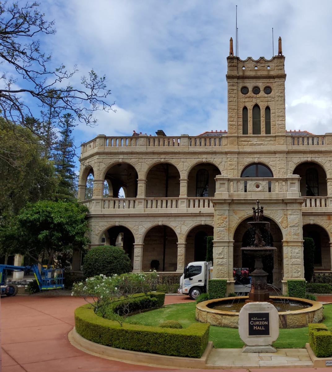 Historic sandstone building with manicured courtyard and professional cleaning vehicle parked outside