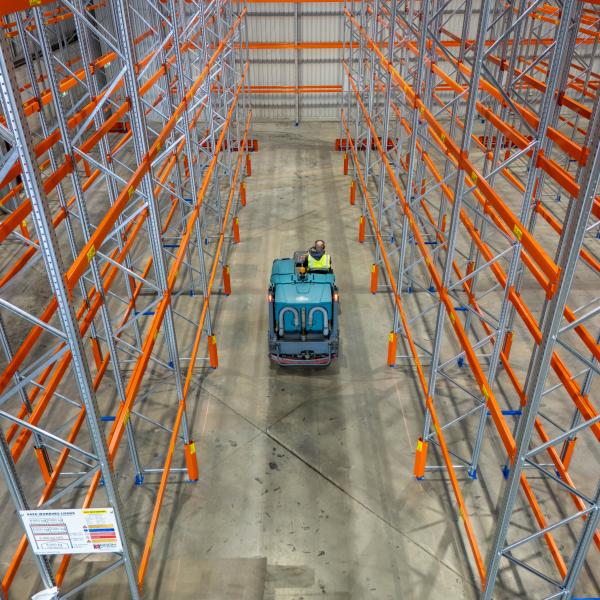 Forklift operator navigating between tall orange racking in warehouse aisle