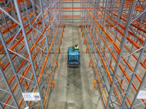 Forklift operator navigating between tall orange racking in warehouse aisle