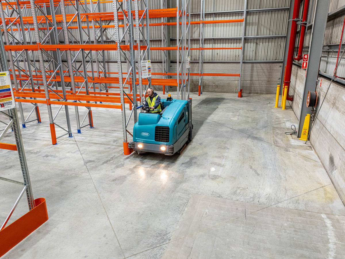 Industrial floor scrubber machine cleaning warehouse concrete floor between storage racks