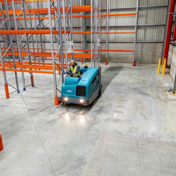 Industrial floor scrubber machine cleaning warehouse concrete floor between storage racks