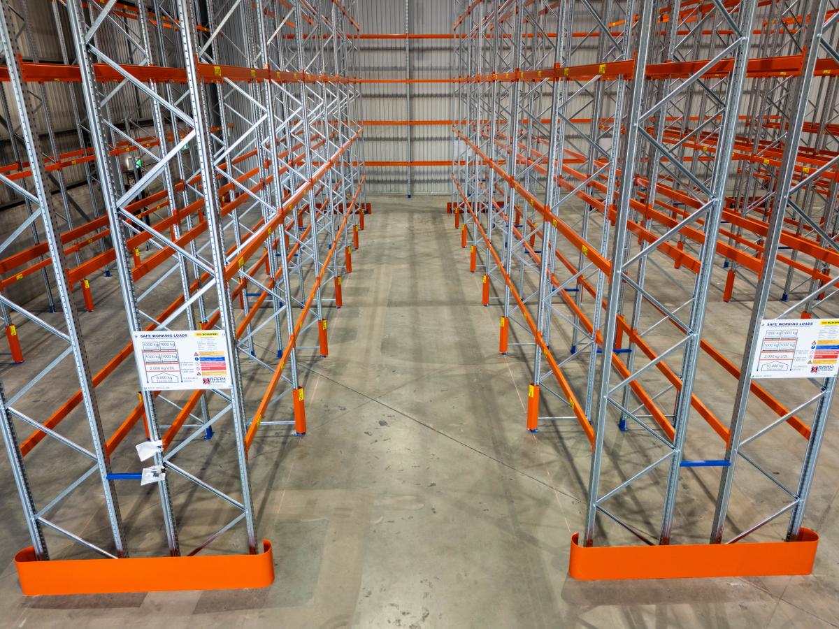Interior view of large industrial warehouse with orange and metal pallet racking system storing goods