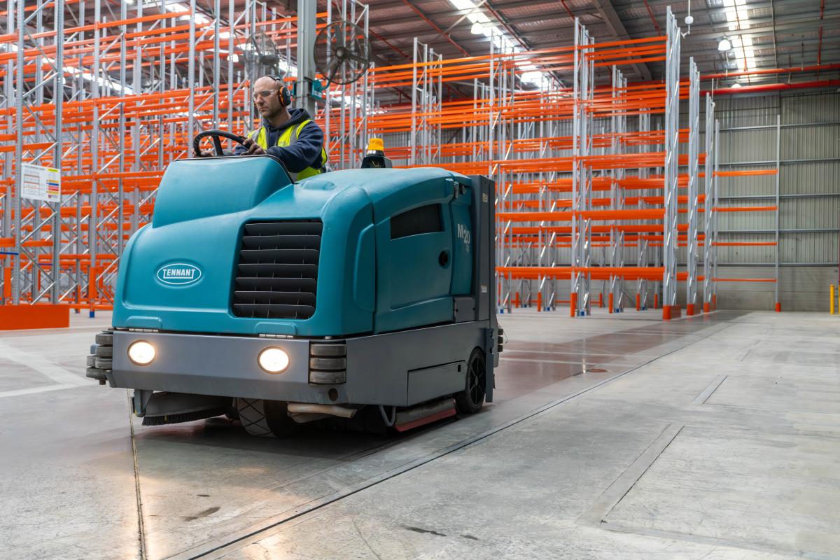 Industrial floor scrubber machine cleaning warehouse floor with pallet racking in background