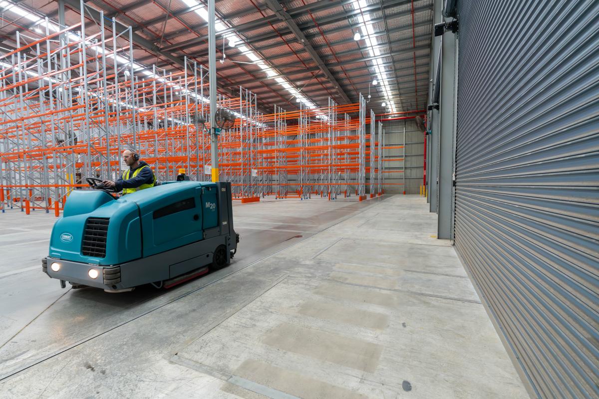 Industrial floor scrubber machine cleaning warehouse concrete floor with pallet racking storage in background