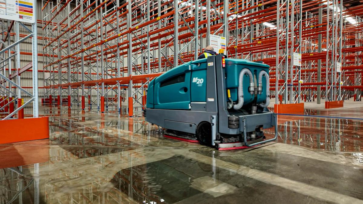 Industrial floor cleaning machine operating in warehouse with pallet racking systems