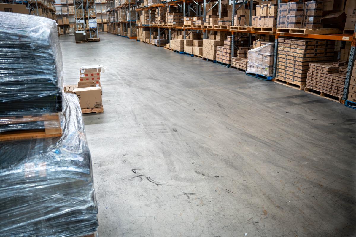 Large warehouse floor with organised storage racks, pallets, and cardboard boxes stacked neatly