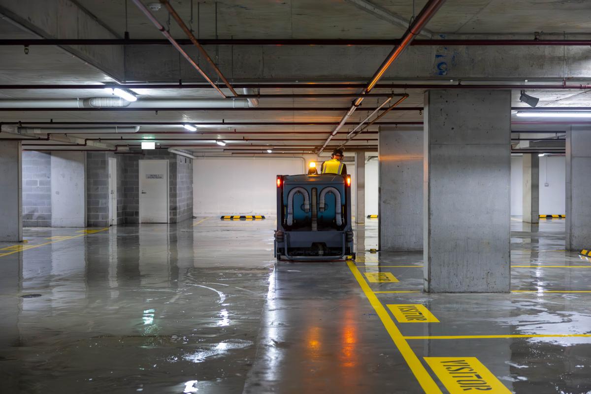Industrial floor cleaning machine operating in underground car park with wet concrete floor and yellow safety markings
